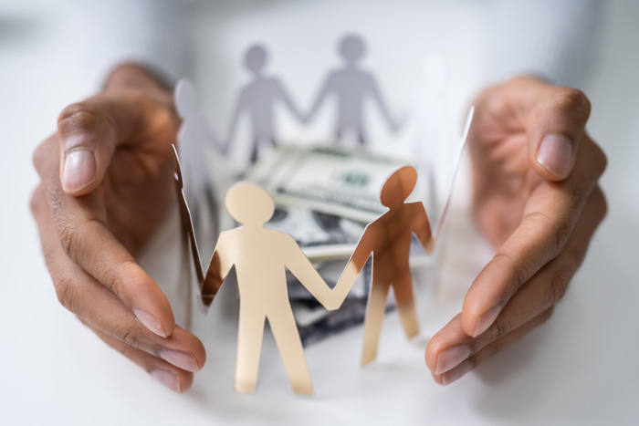 currency and a group of paper dolls surrounded by a man's cupped hands