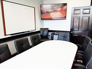 Meeting space with white board, monitor, and executive leather chairs around a conference table